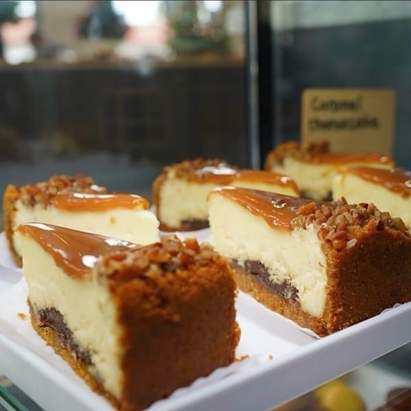 Several slices of caramel cheesecake with nuts on a white tray in a display case.