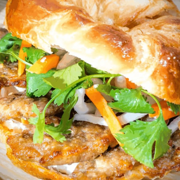 Close-up of a Vietnamese banh mi sandwich with grilled meat, cilantro, and pickled carrots on a croissant.