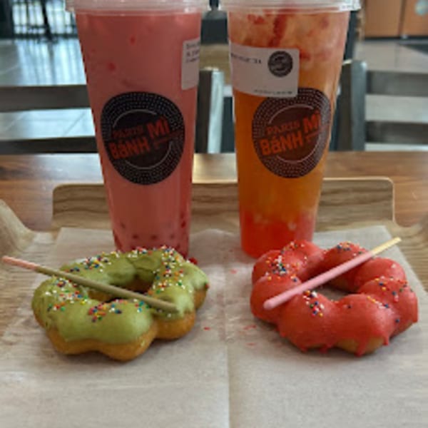 Two Paris Banh Mi bubble teas, one pink and one orange, with green and red mochi donuts.