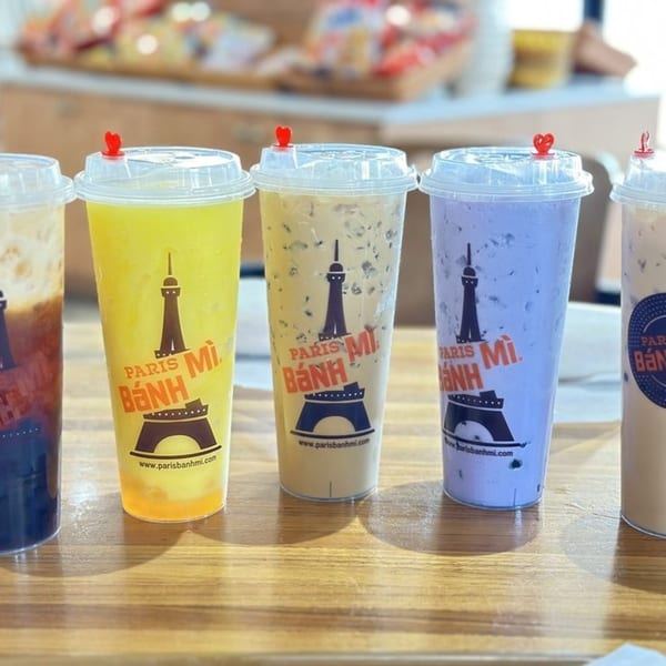 Five colorful Paris Banh Mi drinks with heart-shaped stoppers on a wooden table.