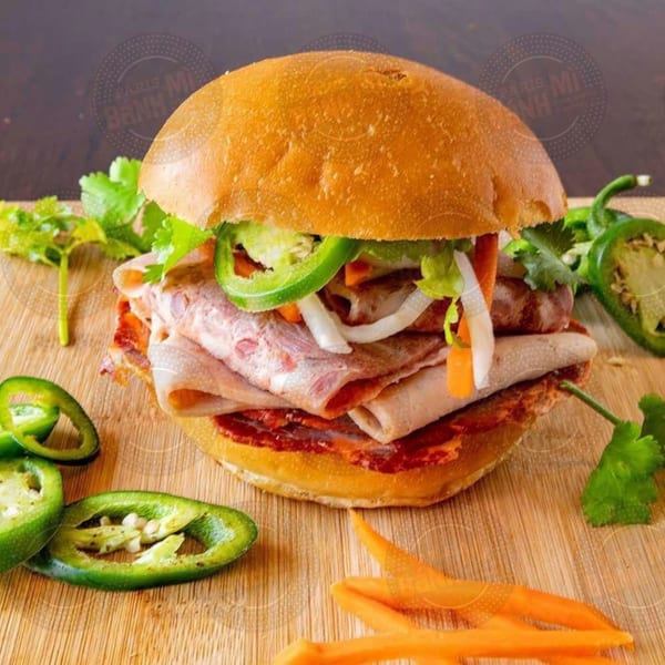 A Vietnamese banh mi sandwich with meat, vegetables, and jalapeños on a wooden board.
