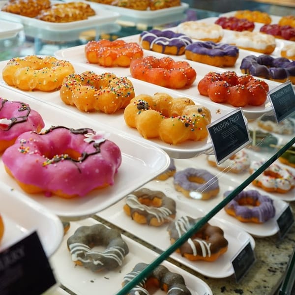Colorful mochi donuts with various glazes and sprinkles displayed in a glass case at Paris Banh Mi.
